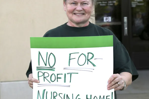 A photo of a woman holding a "no for-profit nursing home" sign