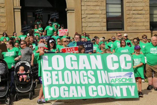 Members holding sign saying Logan CC belongs in Logan County
