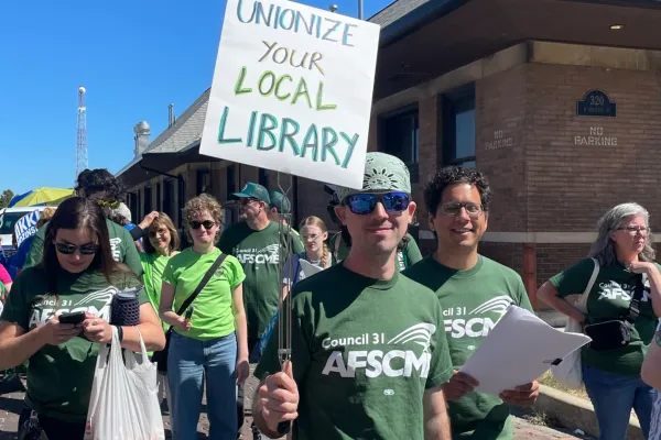 An AFSCME member holding a sign reading "Unionize your local library"