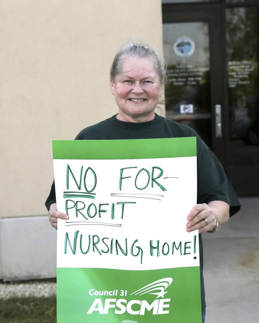 A photo of a woman holding a "no for-profit nursing home" sign